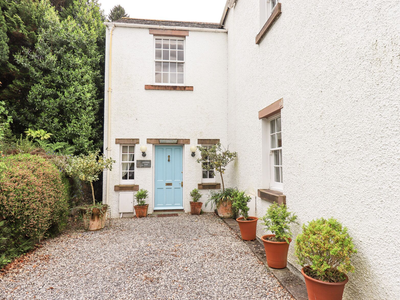 A white building with a blue door, surrounded by gravel and potted plants.