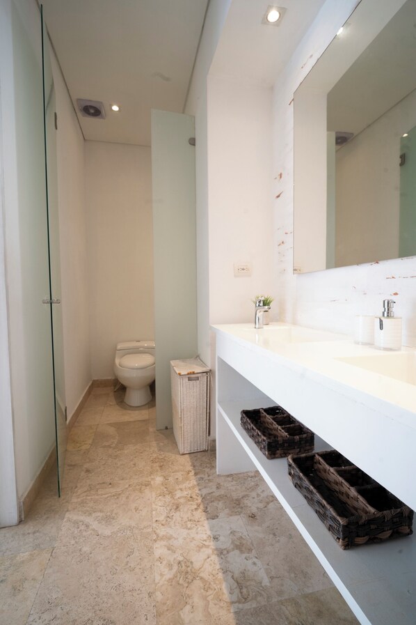 A modern bathroom with a glass shower enclosure, a white toilet, and a large mirror above a white sink with two basins. - Beatiful view in front the sea ,inside old City (Cartagena de Indias)
