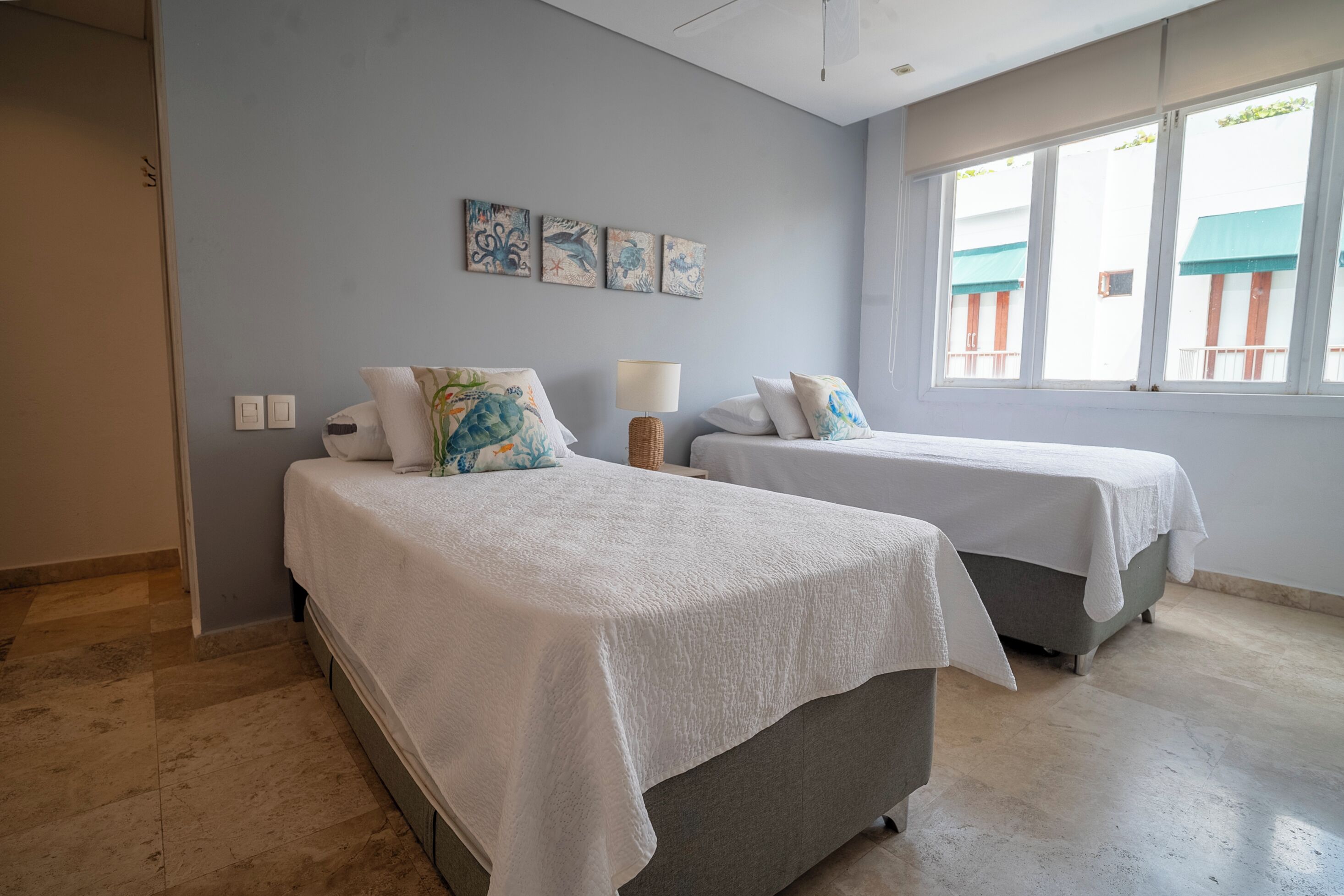 A bedroom with two beds, a window with a view, and artwork on the wall.