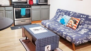 Un espace de vie compact comprenant un coin cuisine, un canapé agrémenté de coussins à motifs et une petite table.