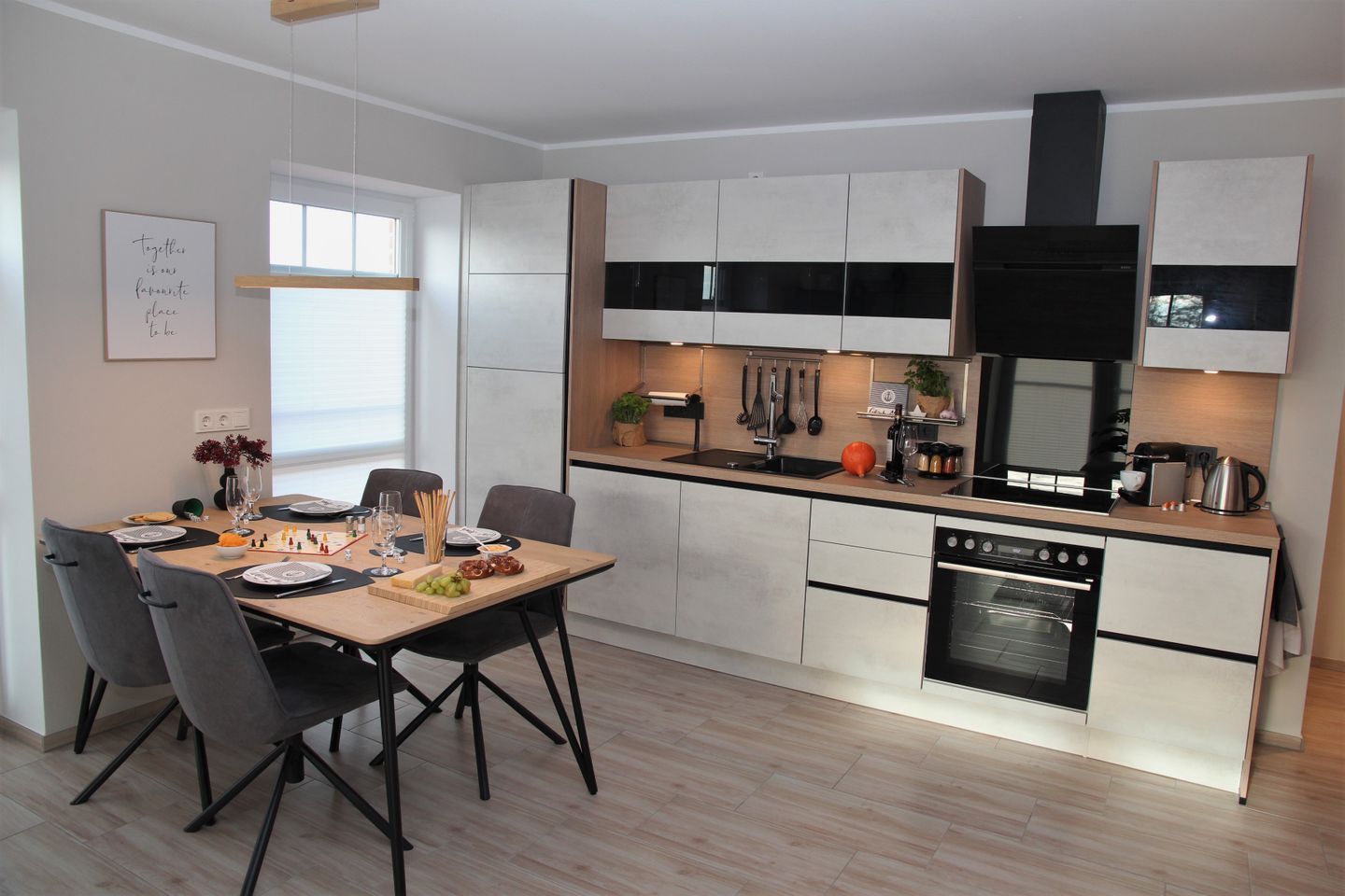 A modern kitchen with white cabinets, a black range hood, and a built-in oven.