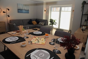 Un coin repas avec un jeu de société, des assiettes, des couverts et des verres sur une table en bois.