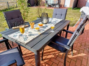 Un espace de restauration en plein air avec une table dressée pour deux personnes, comprenant une assiette, des couverts, des verres et un bol de chips.