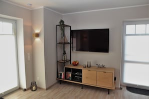 A modern living room with a wooden cabinet, a TV mounted on the wall, and a small plant on a shelf. - Schnack-Stuuv - Great 72sqm apartment for 4 people with terrace in the (Krummhörn)