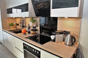 A modern kitchen with a black stovetop, stainless steel appliances, and wooden cabinetry. - Schnack-Stuuv - Great 72sqm apartment for 4 people with terrace in the (Krummhörn)