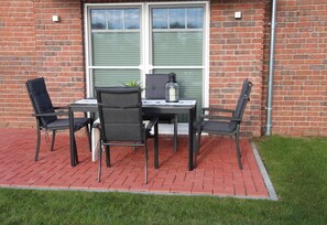 Une terrasse avec une table en briques et quatre chaises, une petite plante et une bougie posée sur la table.