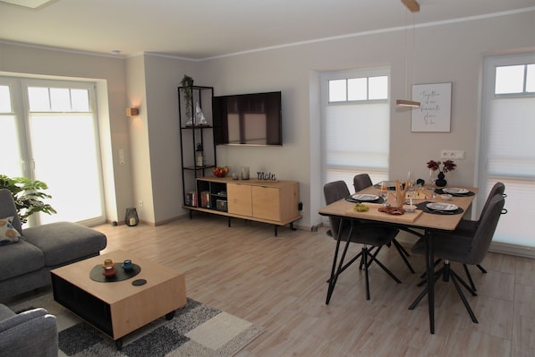Un salon moderne avec un coin repas, comprenant un canapé, une table basse, un meuble en bois et une table à manger avec des chaises pour quatre personnes.