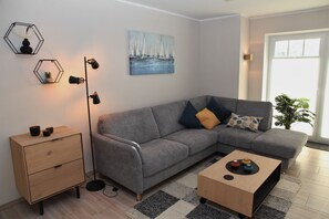 A modern living room with a grey sectional sofa, a wooden coffee table, a floor lamp, and a painting of sailboats on the wall.