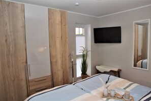 Une chambre à coucher avec un lit, une armoire, une télévision, un miroir et une fenêtre.