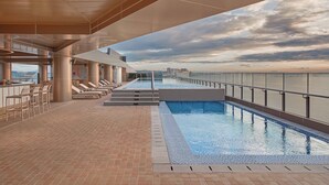 A rooftop pool area with a view of the city skyline, lounge chairs, and a bar area.