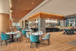 A modern restaurant with round tables, teal chairs, and a central bar area. - Lanson Place Mall of Asia Manila (Pasay)
