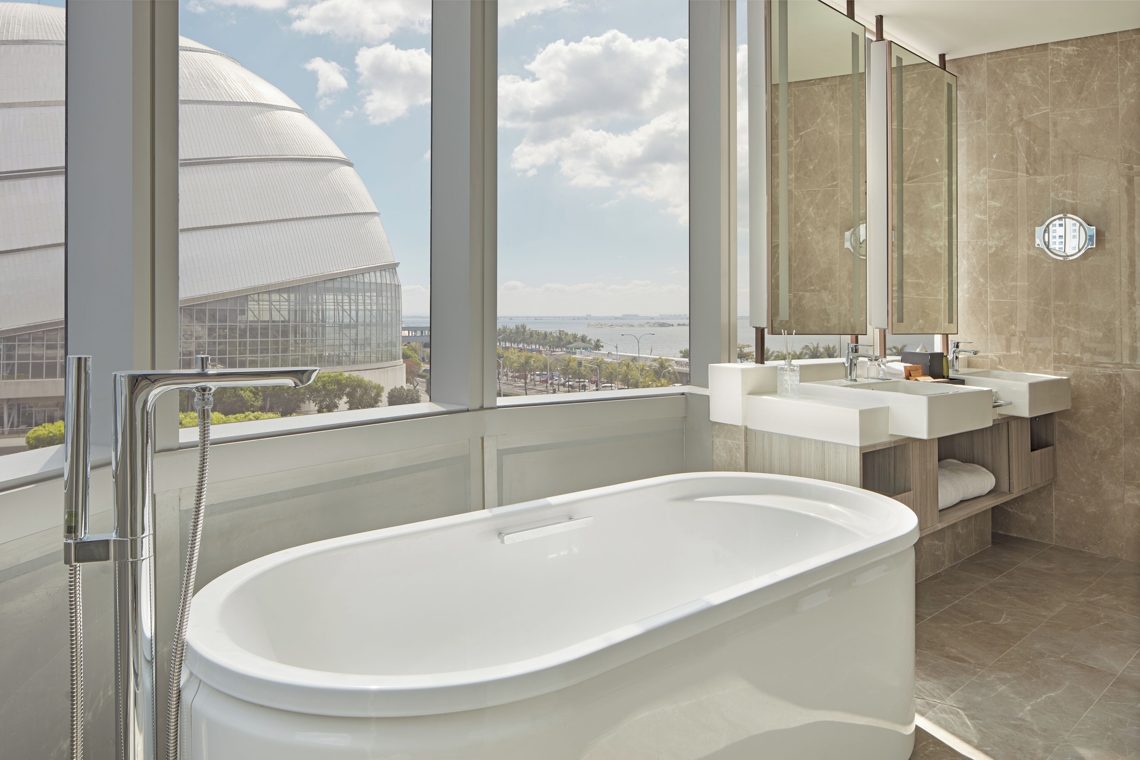 A modern bathroom with a freestanding bathtub, a large mirror, and a view of a cityscape through large windows.
