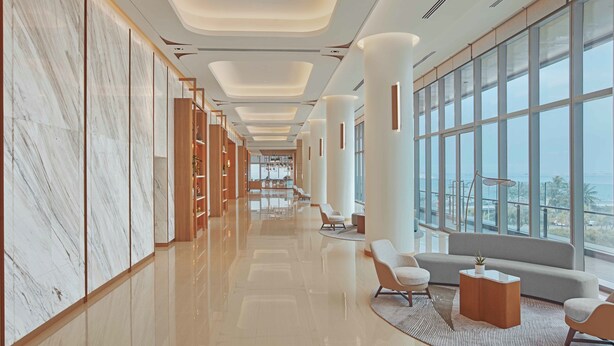 A modern hotel lobby with marble walls, a polished floor, and large windows offering a view.