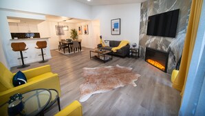 Een moderne woonkamer met een open haard, een eethoek en een keuken op de achtergrond.