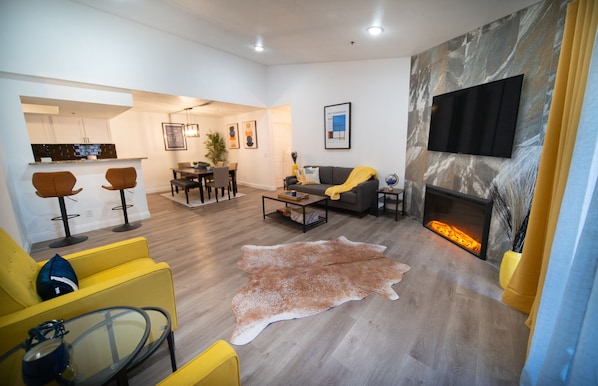 Un salon moderne avec une cheminée, un coin repas et une cuisine en arrière-plan.