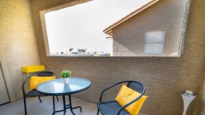 Een klein terras met een ronde tafel en twee stoelen, elk met een gele kussen.
