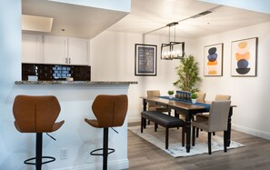 Une cuisine moderne avec un coin bar, une table à manger avec des chaises et des œuvres d’art accrochées aux murs.