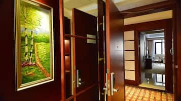 Entrada a una habitación de hotel con puerta de madera, un cuadro de un árbol y un vistazo al interior de la habitación.