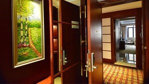 Habitación de hotel con puerta de madera, un cuadro enmarco de un árbol y vista al interior.