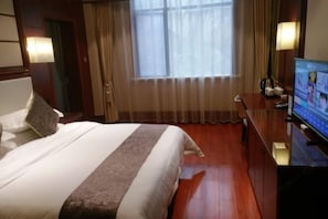 Ein Hotelzimmer mit einem Bett, einem Schreibtisch mit Computer, einem Fenster mit Vorhängen und einer Lampe.