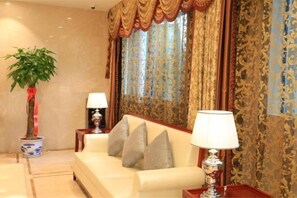 A room with a sofa, two lamps, a potted plant, and patterned curtains. - Fuan International Hotel (Zhuxi)