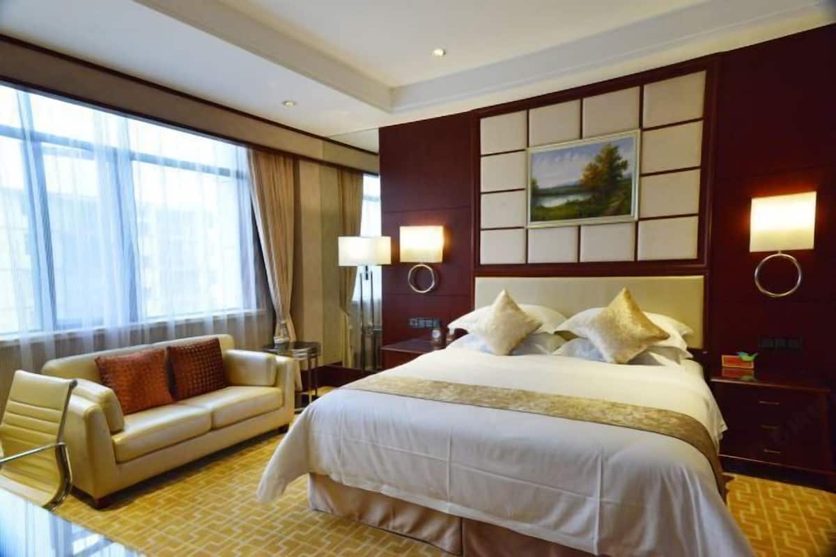 A hotel room with a large bed, a sofa, a desk, and a window with curtains.