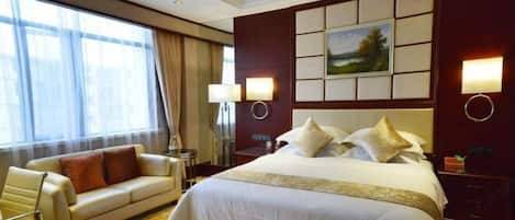 A hotel room with a large bed, a sofa, a desk, and a window with curtains.