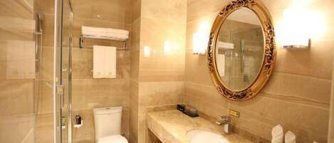 A bathroom with a glass shower enclosure, a toilet, a sink, and a large mirror with an ornate frame.