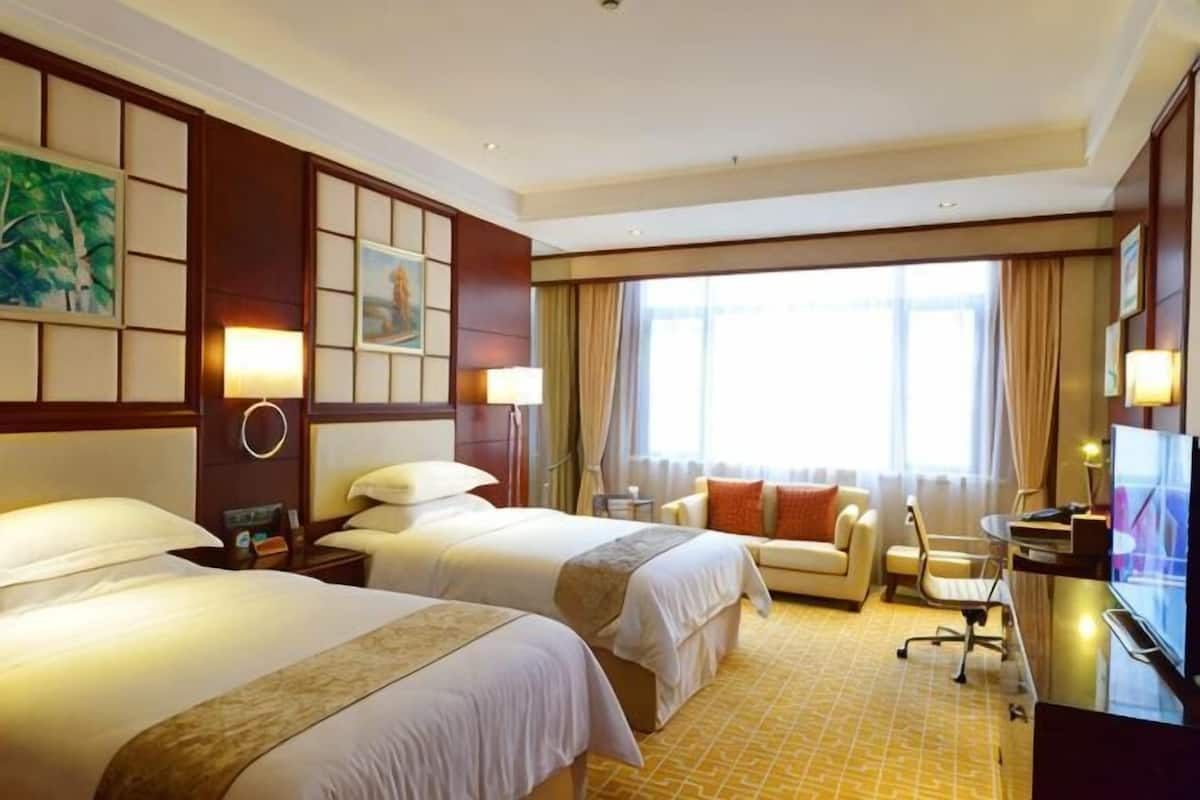 A hotel room with two beds, a sofa, a desk, and a TV.