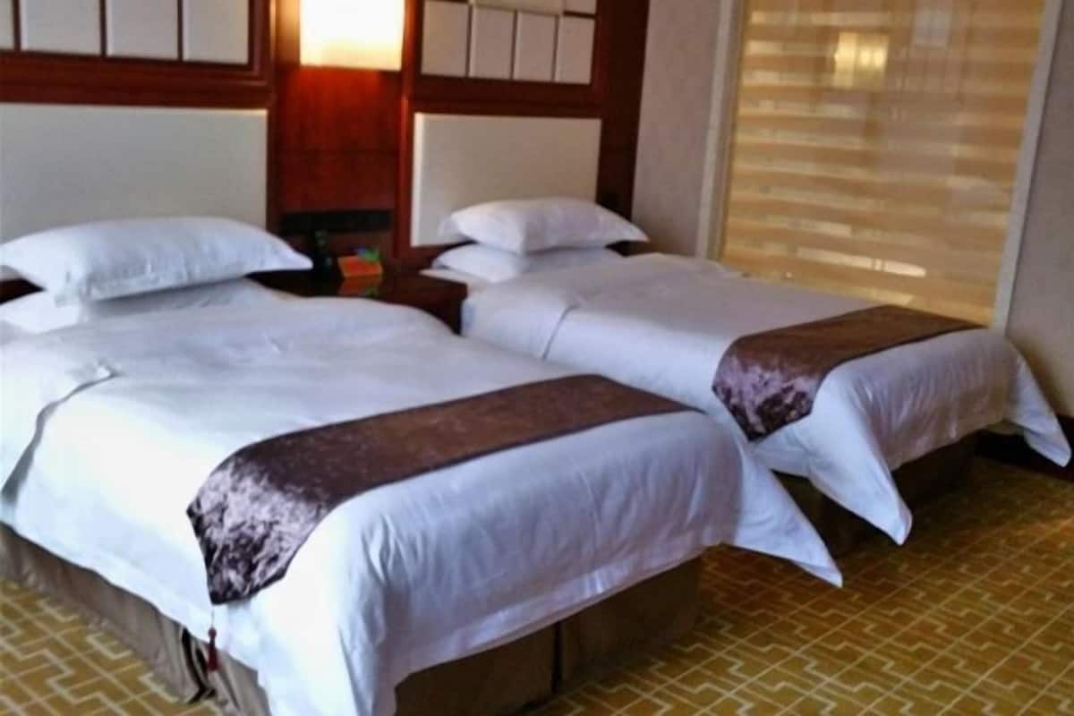 A hotel room with two beds, a wooden headboard, a nightstand, and a patterned floor.