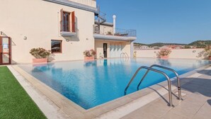 Ein Schwimmbecken mit Metallleiter, ein Gebäude mit Balkon und ein klarer Himmel.