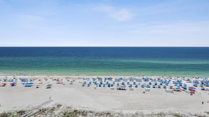 Une plage avec de nombreux parasols et des chaises de plage, un rivage sablonneux et une mer calme sous un ciel dégagé.