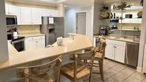 Une cuisine moderne avec des armoires blanches, des appareils en acier inoxydable et un îlot central doté de chaises.