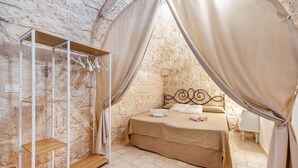 A bedroom with a stone wall, a canopy bed, a wooden wardrobe, and a small bedside table. - Trullo Delle Ginestre Private Pool, Latiano, Italy (Latiano)