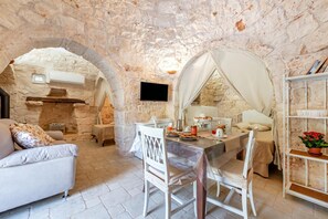 Une pièce aux murs de pierre, comprenant une table à manger, des chaises, un canapé, un téléviseur et une bibliothèque.