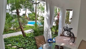 A glass table with two candles, a bicycle, and a view of a swimming pool and greenery. - CONDO GAVIOTAS II DEP 105 (Playa del Carmen)