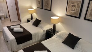 A hotel room with two beds, each with a white and brown bedspread, a remote control, and a lamp on the nightstand. - CONDO GAVIOTAS II DEP 105 (Playa del Carmen)