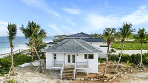 Een huis aan het strand met een balkon, een trap naar de ingang en uitzicht op de oceaan.