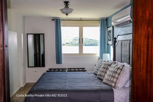 Un dormitorio con cama, ventana con cortinas, luz de techo y vistas a una colina.