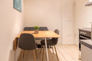 Una cocina compacta con una mesa y sillas de madera, una planta pequeña en maceta y un armario blanco.