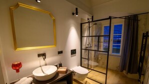 Un baño moderno con un espejo grande, un lavabo redondo, un inodoro y una zona de ducha con mampara de vidrio.