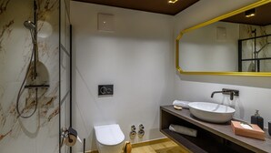Une salle de bain moderne avec un mur en marbre, une douche en verre, des toilettes blanches, un meuble-lavabo en bois et un grand miroir.