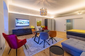 Ein modernes Wohnzimmer mit Flachbildfernseher, einem Esstisch mit Stühlen, einer Couch und einem dekorativen Kronleuchter.