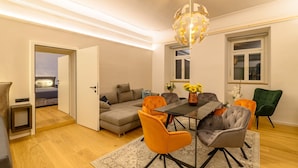 A modern living room with a dining area, a sofa set, a chandelier, and a view through an open door. - Apartment "Gasthof Alte Post - Top 4 Commodore" (Gmünd in Kärnten)