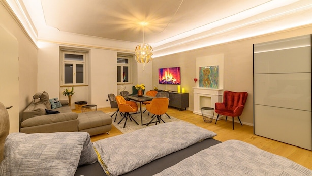 A modern living room with a sofa, ottoman, dining table, chairs, and a fireplace. - Apartment "Gasthof Alte Post - Top 4 Commodore" (Gmünd in Kärnten)
