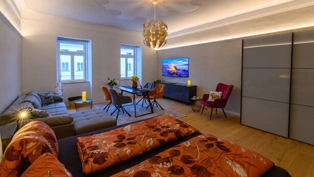 Ein modernes Wohnzimmer mit einer Couch, einem Esstisch, Stühlen, einem Fernseher und einem großen Fenster.
