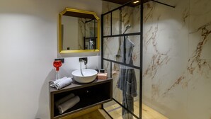 Ein modernes Badezimmer mit Marmorwand, Waschbecken in Weiß, Spiegel mit goldener Rahmung, Handtuchhalter und Duschbereich.