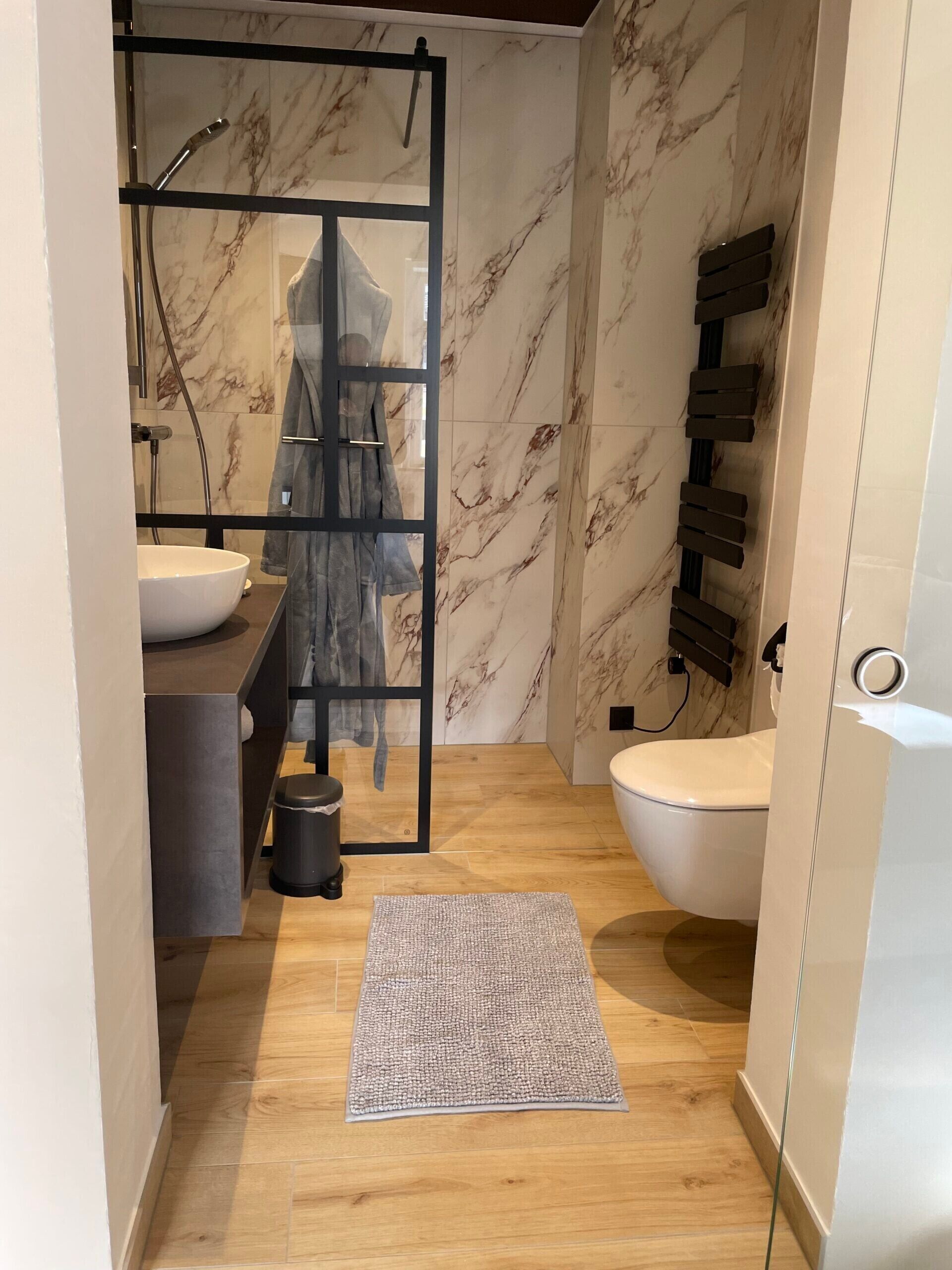 Un bagno moderno con rivestimento in marmo, cabina doccia in vetro, water bianco e lavandino.