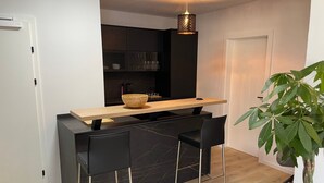 Eine kleine Küche mit einer Holztresen, zwei schwarzen Barhocker, einer Hängelampe und einem Topf mit Pflanze.