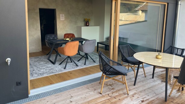 Ein modernes Interieur mit einer Schiebetür zu einem Essbereich, einem kleinen Tisch mit Stühlen und Blick ins Freie.